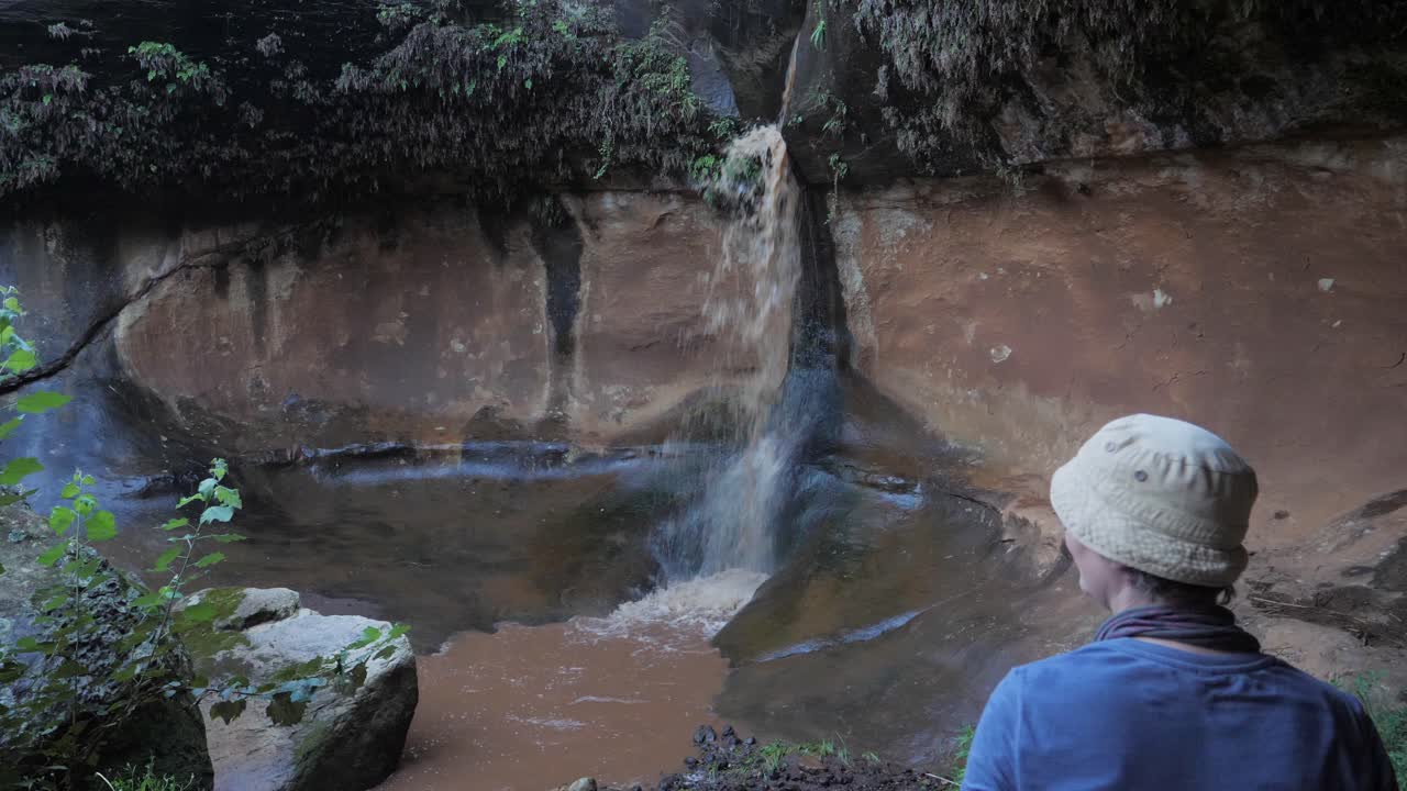 모자를 입은 레소토 관광객 은  ⁇ 드폰 으로 진 ⁇  한 폭포 의 사진 을 찍는다