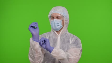 Young-healthcare-worker-doctor-standing-on-chroma-key-and-puts-on-hand-gloves,-coronavirus-pandemic