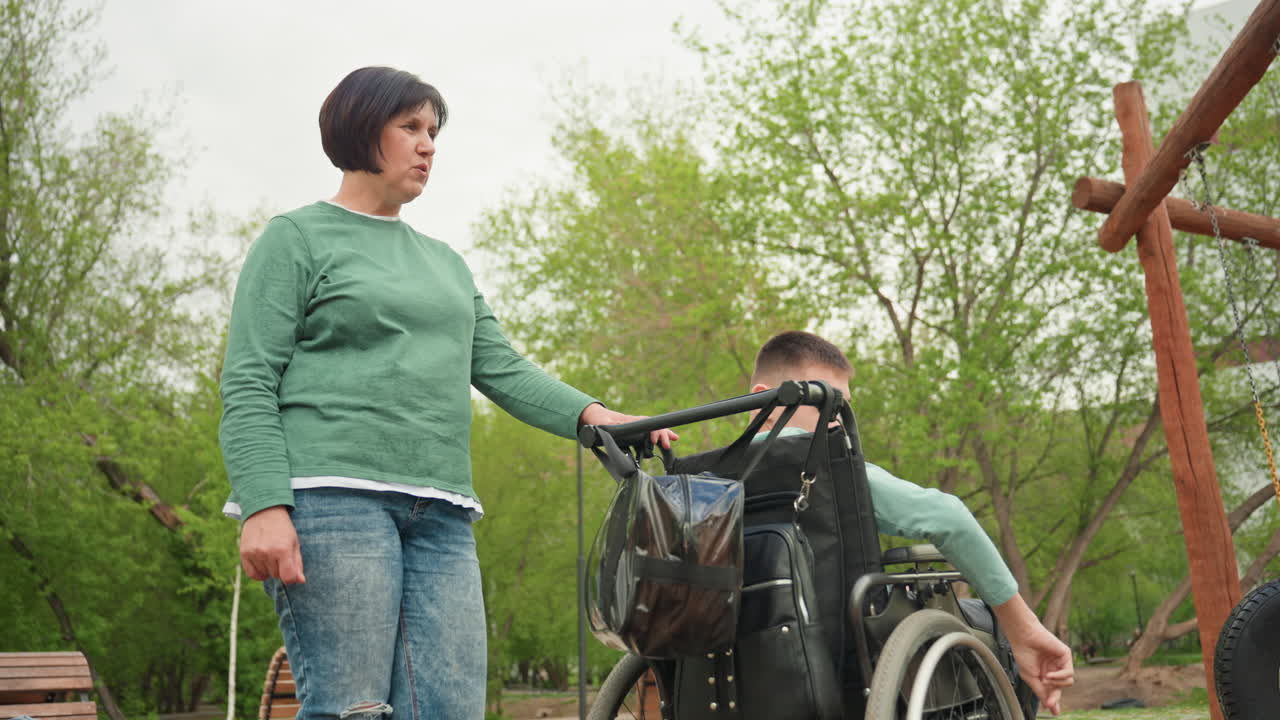 Kind Supporter Guides Youth Outside, Compassionate Person Assists Teen In Wheelchair Outside, Empathetic Helper Encourages Wheelchair User To Experience Tranquil Park Surroundings With Support