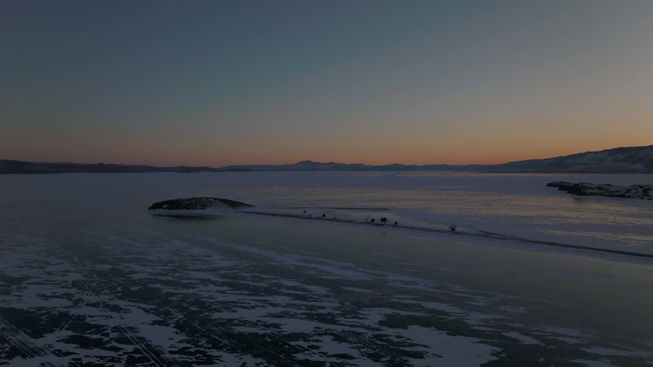 Luftoptagelser af den frosne Bajkalsø ved solnedgang med glat is, sprækker og sne-teksturer, fjerne bjerge og rolig horisont i Sibirien, Rusland, vinterlandskab
