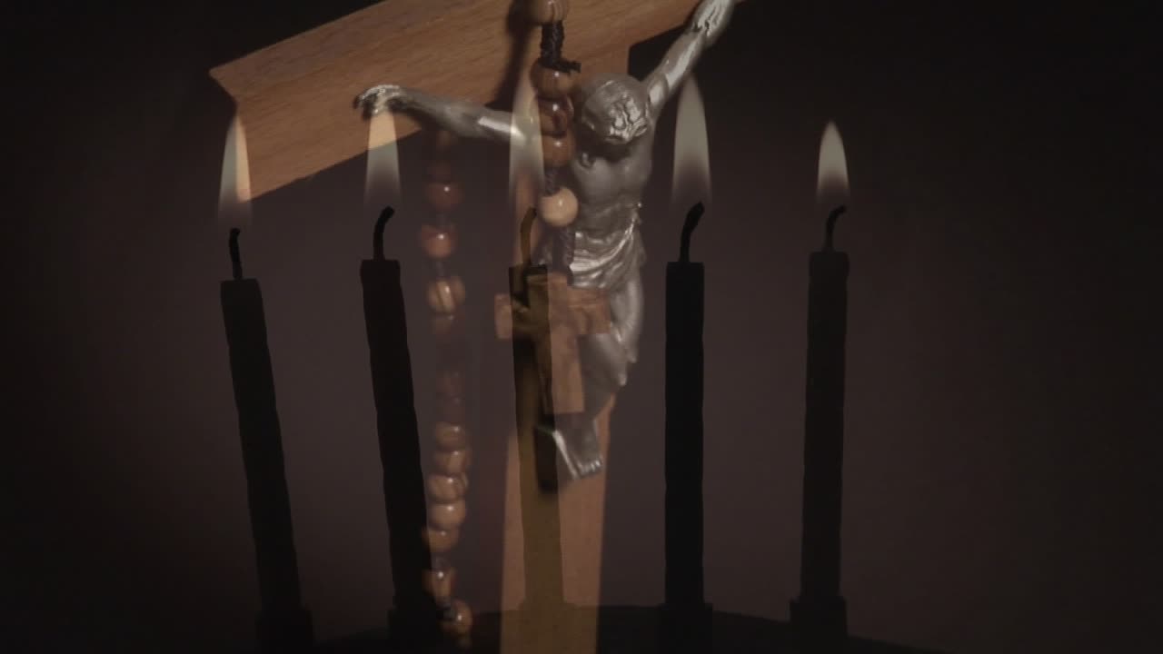 Video composito di candele accese con un primo piano di una croce su sfondo grigio.