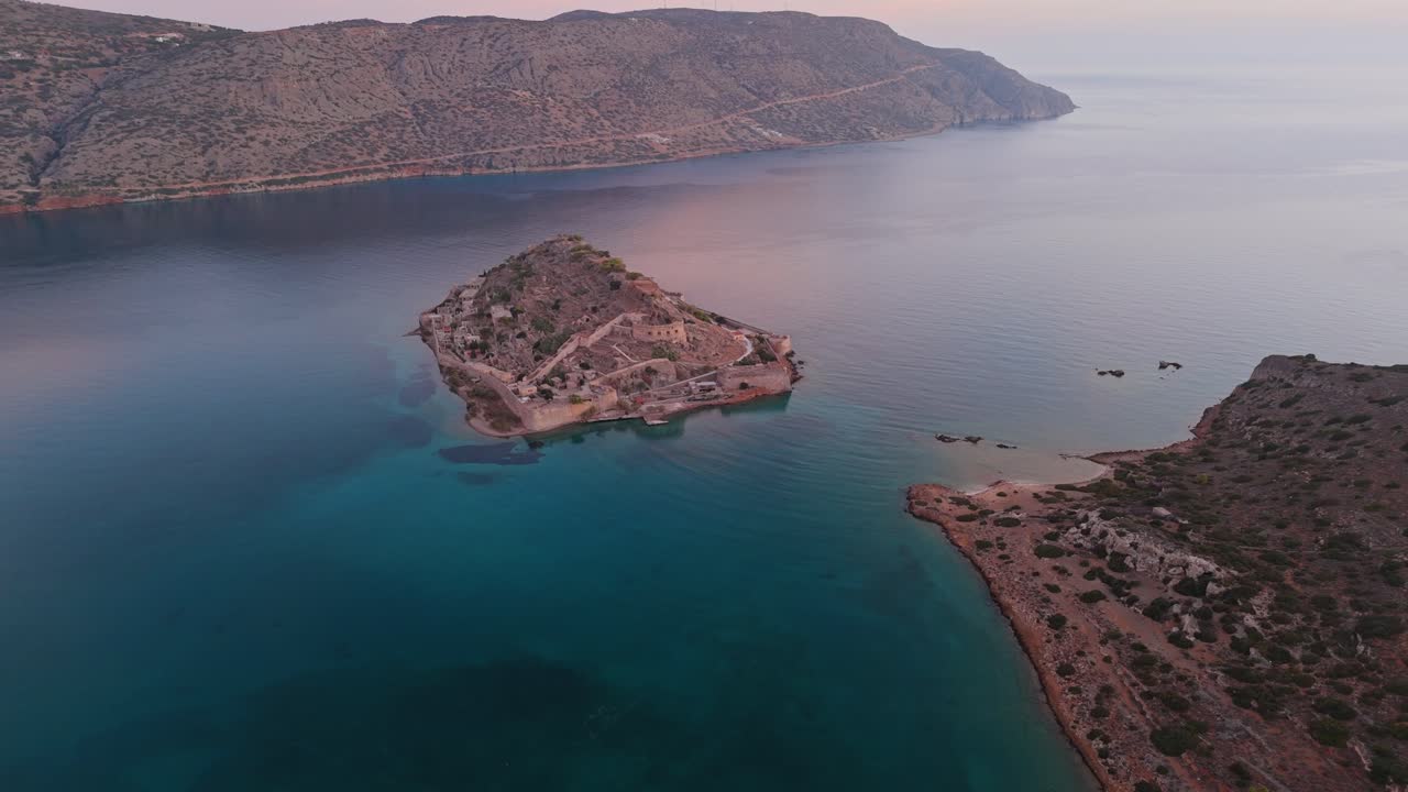 Panoramic aerial establishing overview of Spinalonga island under soft sunset glow