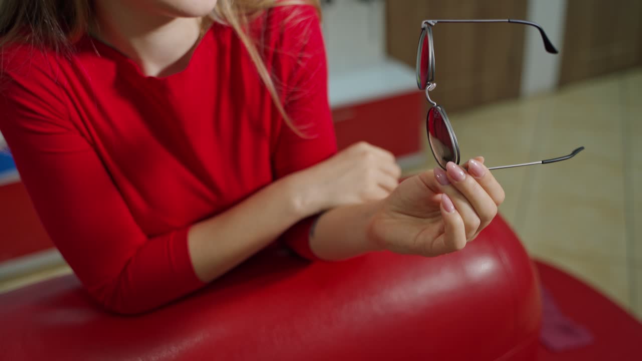 Stylish sunglasses in woman's hands. Girl sits in armchair and holds new trendy black glasses. Close-up. Eyesight concept.