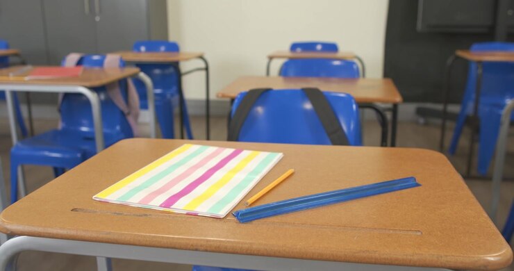 La telecamera si sposta e rifocalizza vicino a un banco di scuola per evidenziare un quaderno pastello, una matita e un astuccio.