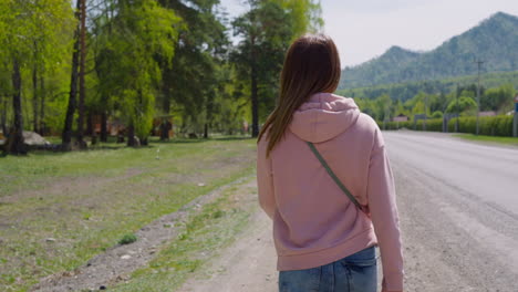 woman in pink hoodie walks along rural road at eco resort