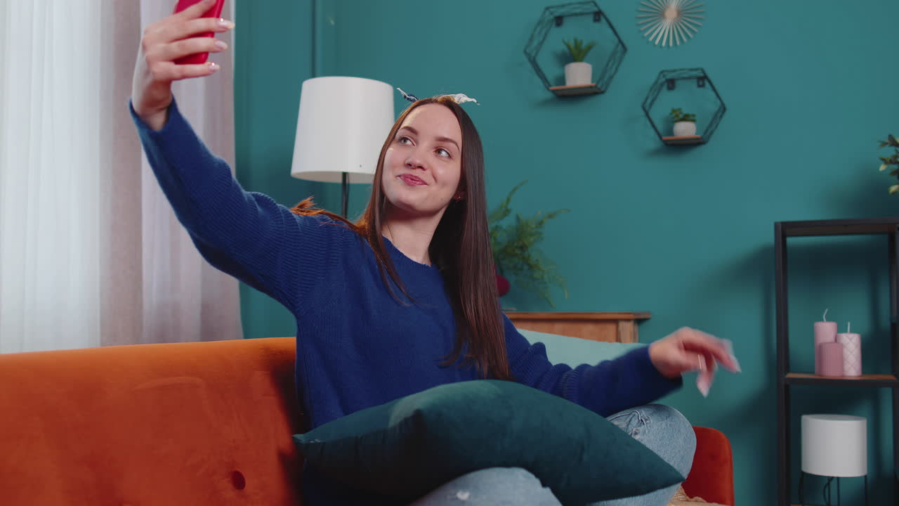 Donna sul divano a casa con lo smartphone che si fa un selfie con la fotocamera del cellulare, videochiamata virtuale online