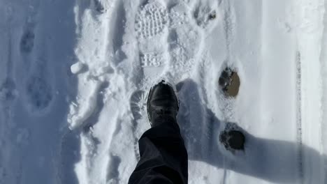 Person-with-black-boots-walking-on-a-snow-covered-sidewalk-on-a-sunny-day