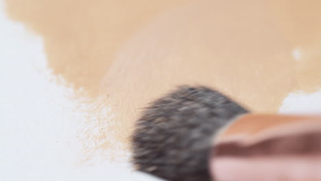 A-close-up-view-of-a-small-brush-making-gentle-strokes-while-applying-a-brown-substance-on-a-white-textured-surface-covering-the-whole-area