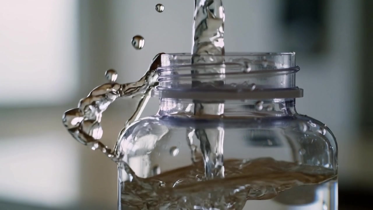 Receiving steady stream from above, clear plastic jar filling on countertop near bright window