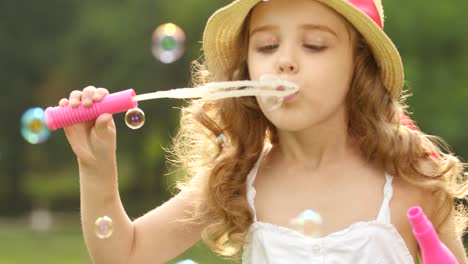 little girl in a beautiful dress holds soap bubbles in her hands and lets them little girl sits on the nature in the park in a beautiful dress and hat holds soap bubbles in her hands and puts them on top