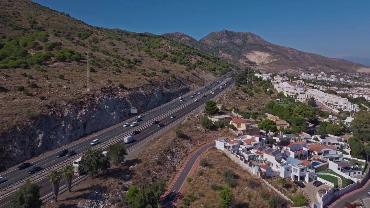 Filmato drone di Benalmádena, Andalusia, con un'autostrada di montagna, ville bianche sulla collina e un movimento in avanti cinematografico sotto cieli sereni.