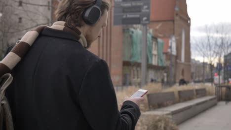 stylish guy in scarf and coat listen a music on streaming service by using mobile phone