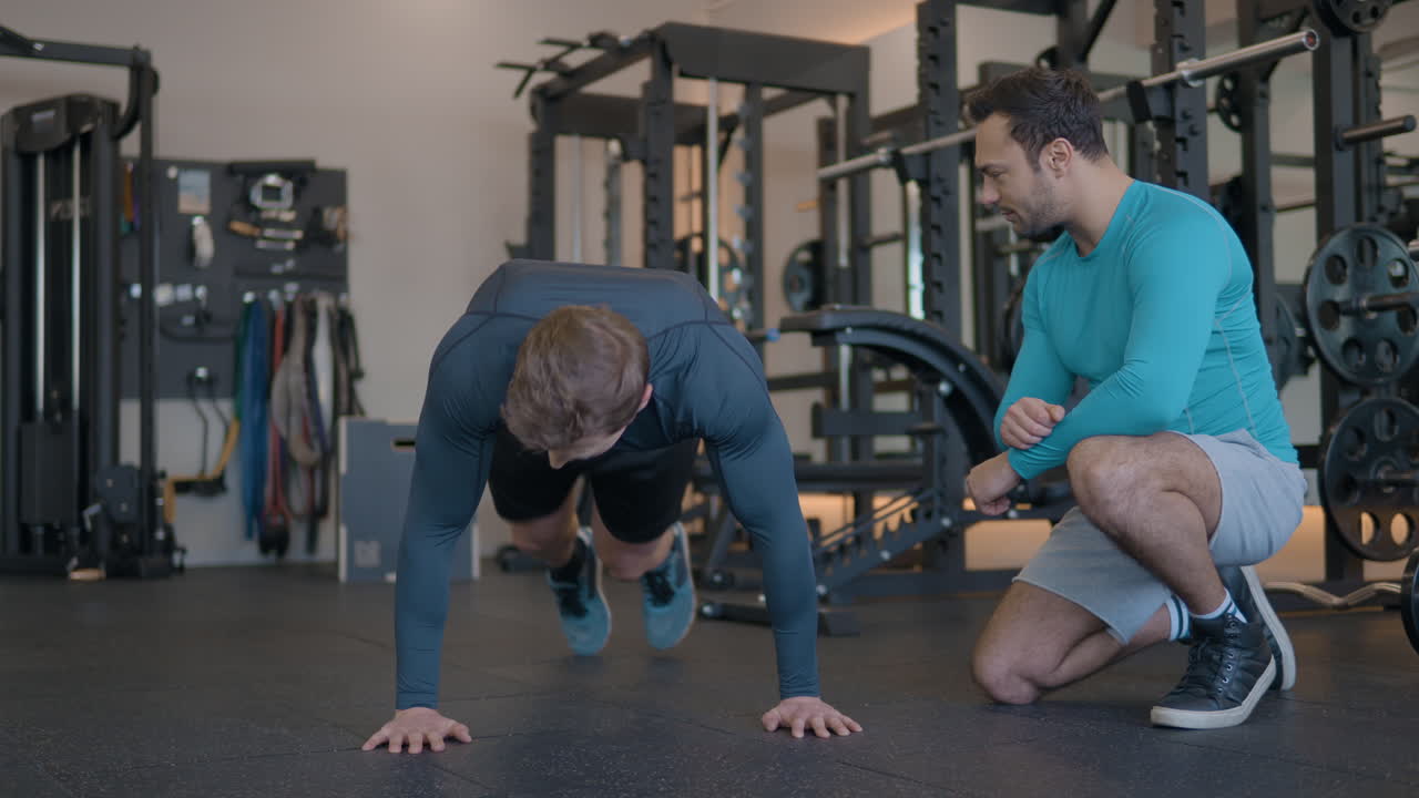deportista en el gimnasio haciendo saltos de tabla lateral bajo la supervisión de un entrenador personal en cámara lenta