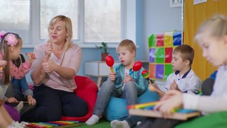 children leisure, boys with disabilities play on maracas with kids and teacher during music lesson sitting on multicolored bean bag chairs