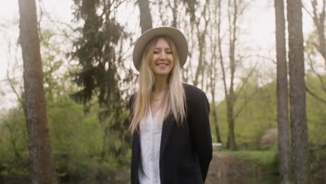 portret van een gelukkige blonde vrouw met hoed die in het park staat en naar de camera kijkt 2