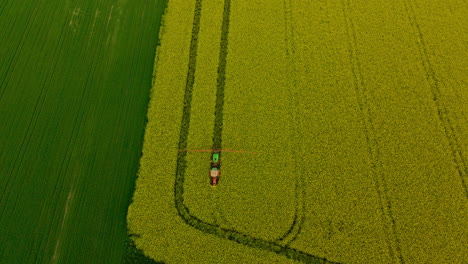 Tractor-Agrícola-Con-Brazos-Rociadores-Rociando-Pesticidas-Sobre-Un-Campo-De-Colza-En-Flor-Amarilla,-Retroceso-Aéreo