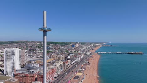 drone orbit of the i360 tower in brighton on a sunny day. city life, beachgoers, and swimmers captured in vibrant coastal atmosphere