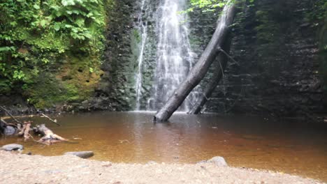 Drohnenflug-Einen-Wasserfall-Hinunter-Und-Dann-Tief-Nach-Hinten,-Um-Baumstämme-Und-Niedrige-Wasserstände-Im-Sommer-Zu-Enthüllen