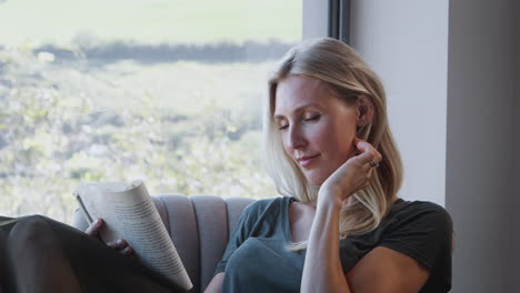 Frau-Entspannt-Sich-Zu-Hause-Im-Stuhl-Am-Fenster-Und-Liest-Ein-Buch