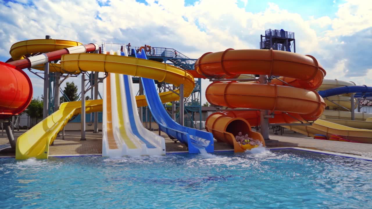 Beautiful aquapark under blue sky. Colorful slides with clear water in the swimming pool outdoors. Joyful entertainment in the open air in a summertime.