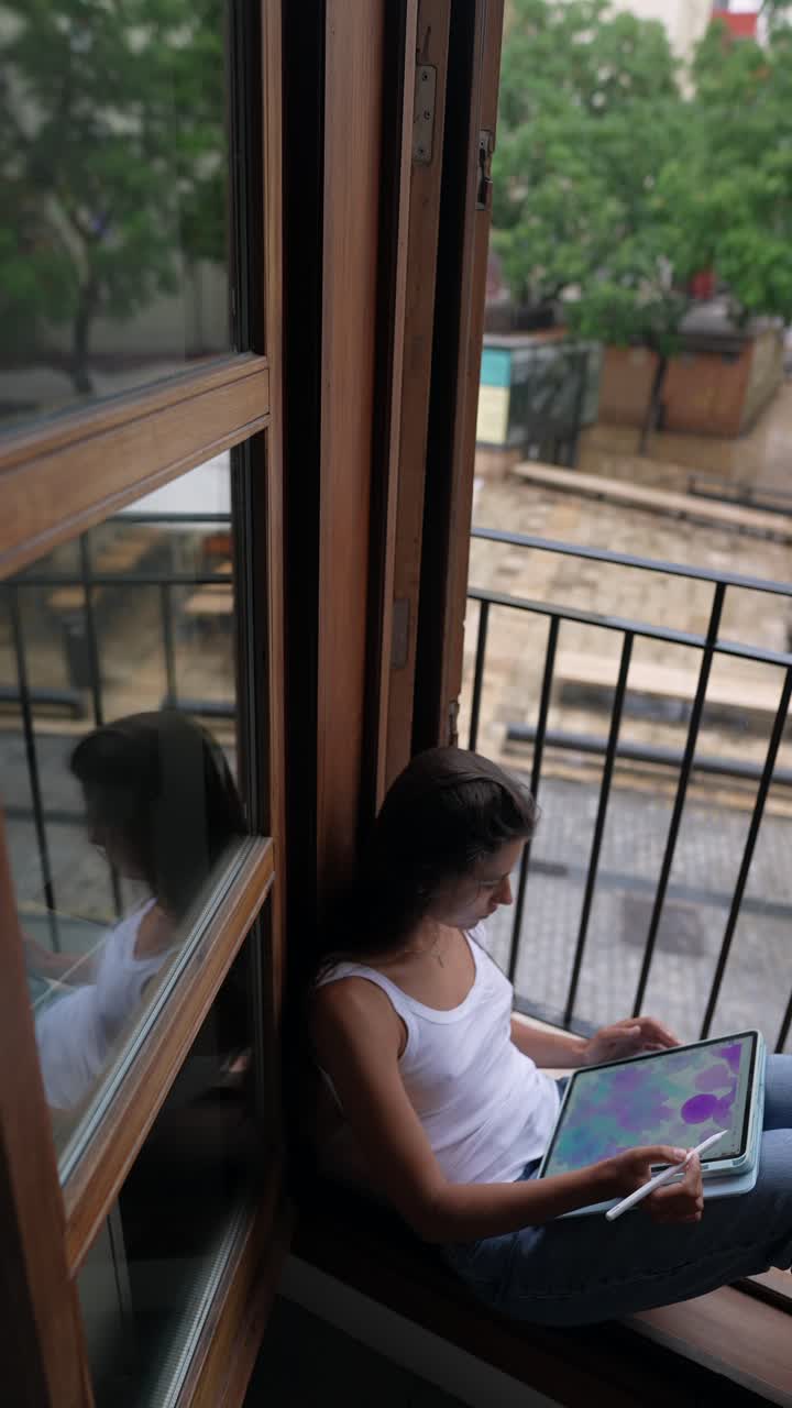 mujer dibujando en la tableta en una ventana de la ciudad lluviosa