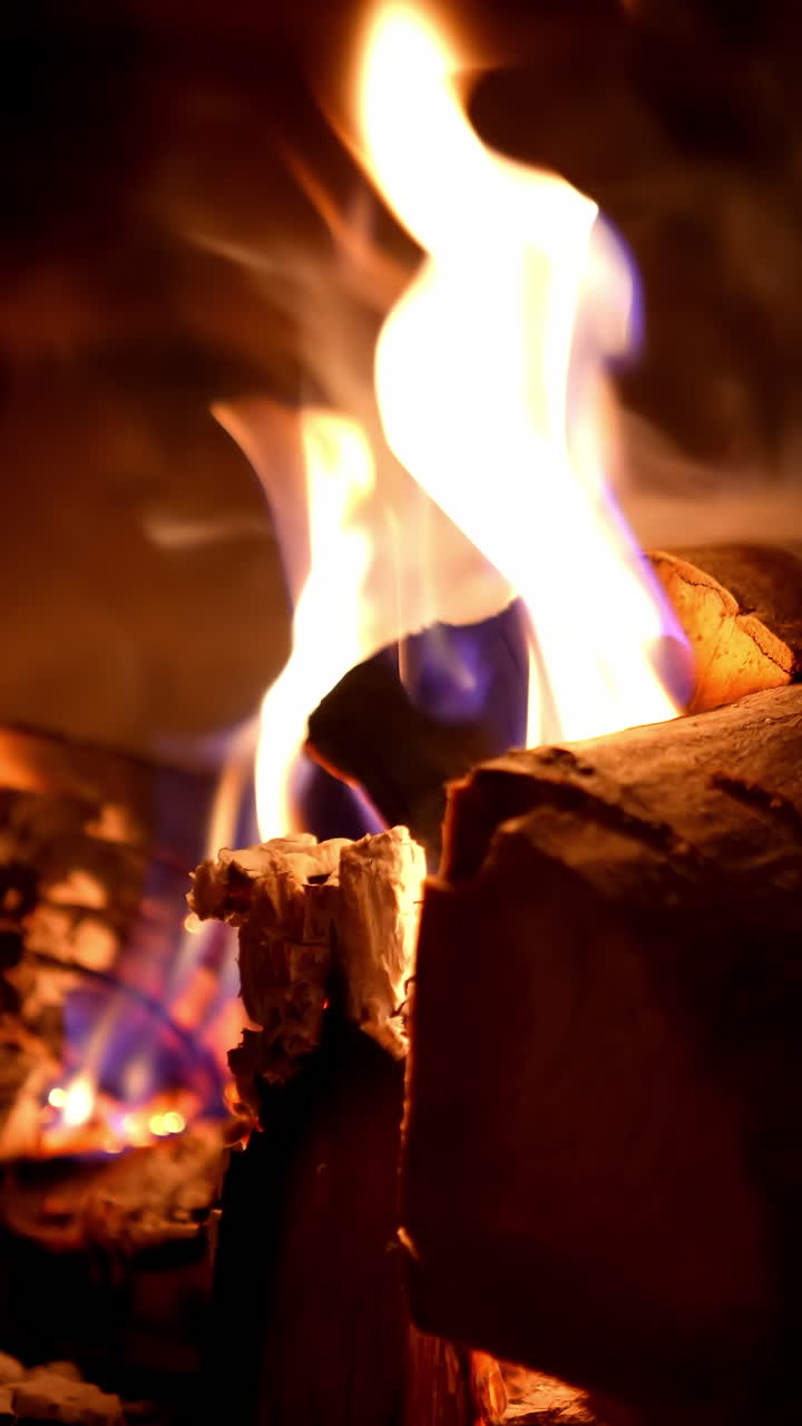 Firewood burning background. Fire flame and smoke on wooden logs in fireplace. Warmth and relaxation near the fireplace at winter season. Close-up. Vertical video