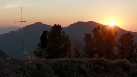 aerial orbiting hiker standing on mountain peak at sunset in the backcountry