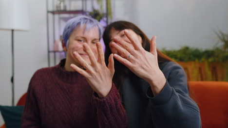 Two-young-lesbian-LGBT-women-family-couple-showing-engagement-rings-after-wedding-on-hands-at-home