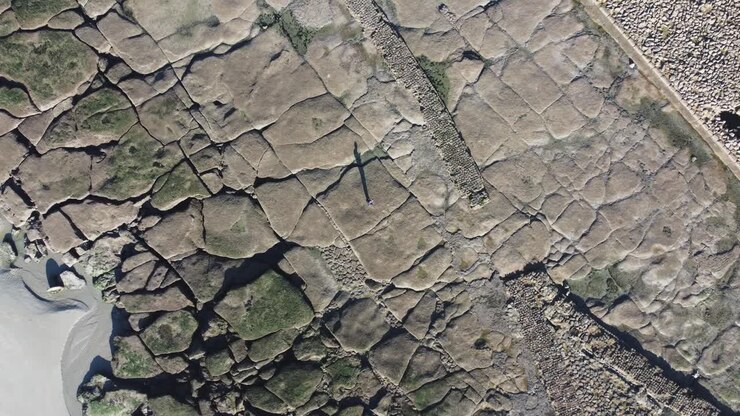 Rotating bird's eye view of a man's shadow on a sandy and rocky beach near Wimereux and Boulogne-sur-Mer