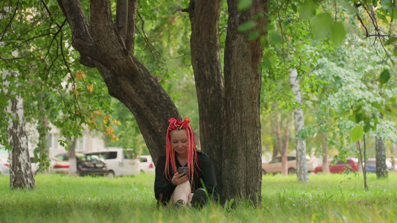 나뭇잎이 무성한 나무 아래에서 휴식을 취하는 여성, 도시 환경의 푸르른 나무 아래에서 평화로운 휴식을 취하는 여성, 번잡한 도시 환경 속에서 나뭇가지 아래에서 조용한 휴식을 취하는 외로운 여성