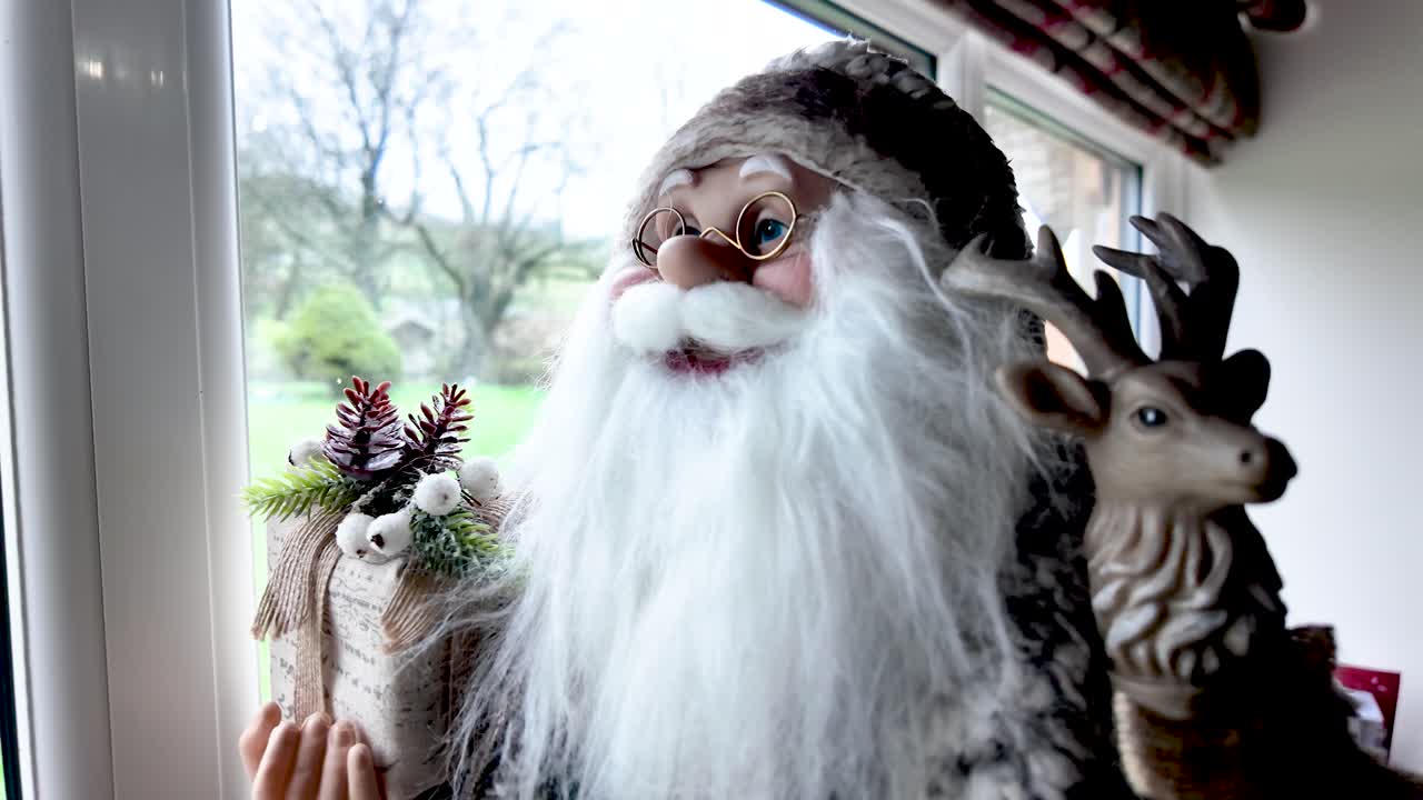 Figurka Santa Clause stojící u okna, držící slavnostní dárek a malého soba