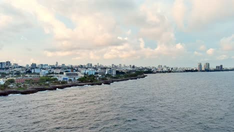 Aerial-view-over-the-ocean,-towards-the-Malecon-and-the-Santo-Domingo-city,-sunset-in-Dominican-Republic