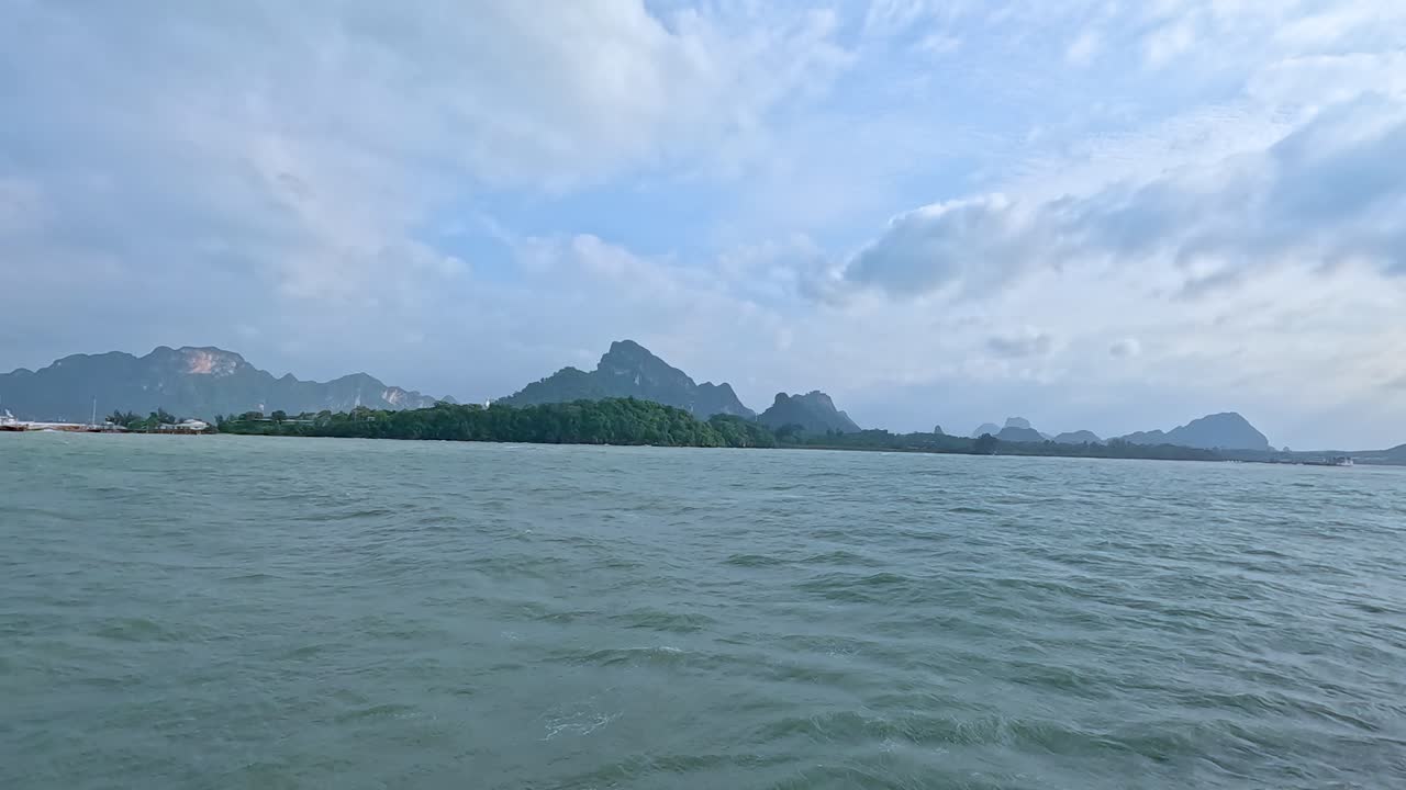 Calm ocean waves and distant mountains under a partly cloudy sky, captured from a moving boat near Koh Samui