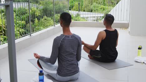 mixed race gay male couple standing on terrace practicing yoga meditating
