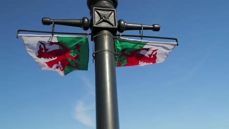 flag of wales - baner cymru - two welsh flags flutter in the breeze with a deep blue sky behind, slomo 60fps