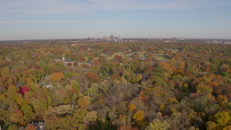 Sobrevuelo-De-árboles-De-Otoño-Con-Una-Pequeña-Iglesia-Y-Un-Horizonte-De-La-Ciudad-En-El-Horizonte