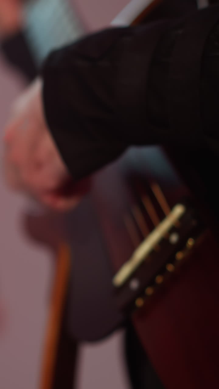 Close-up of a guitarist's hand strumming a red guitar, with a blurred silhouette of a singer in the background, set against a softly focused colorful backdrop
