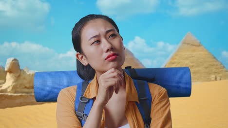 close up of asian female hiker with mountaineering backpack thinking about something and looking around while traveling in pyramid of giza