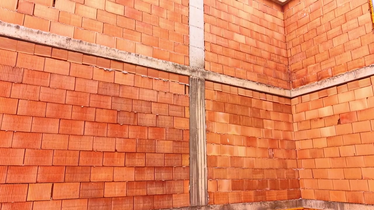 Primo piano di un muro in mattoni ceramici arancioni con struttura in cemento. Dettaglio ravvicinato di una parete di edificio realizzata con blocchi di argilla arancioni sorretti da pilastri e travi in cemento.