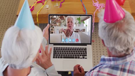 Caucasian-senior-couple-on-laptop-video-chat-wearing-party-hats-at-home