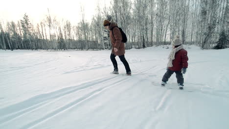 ojciec i syn w śniegu w zimowych ubraniach, ojciec ciągnie dziecko na snowboardzie złapanym liną na zewnątrz