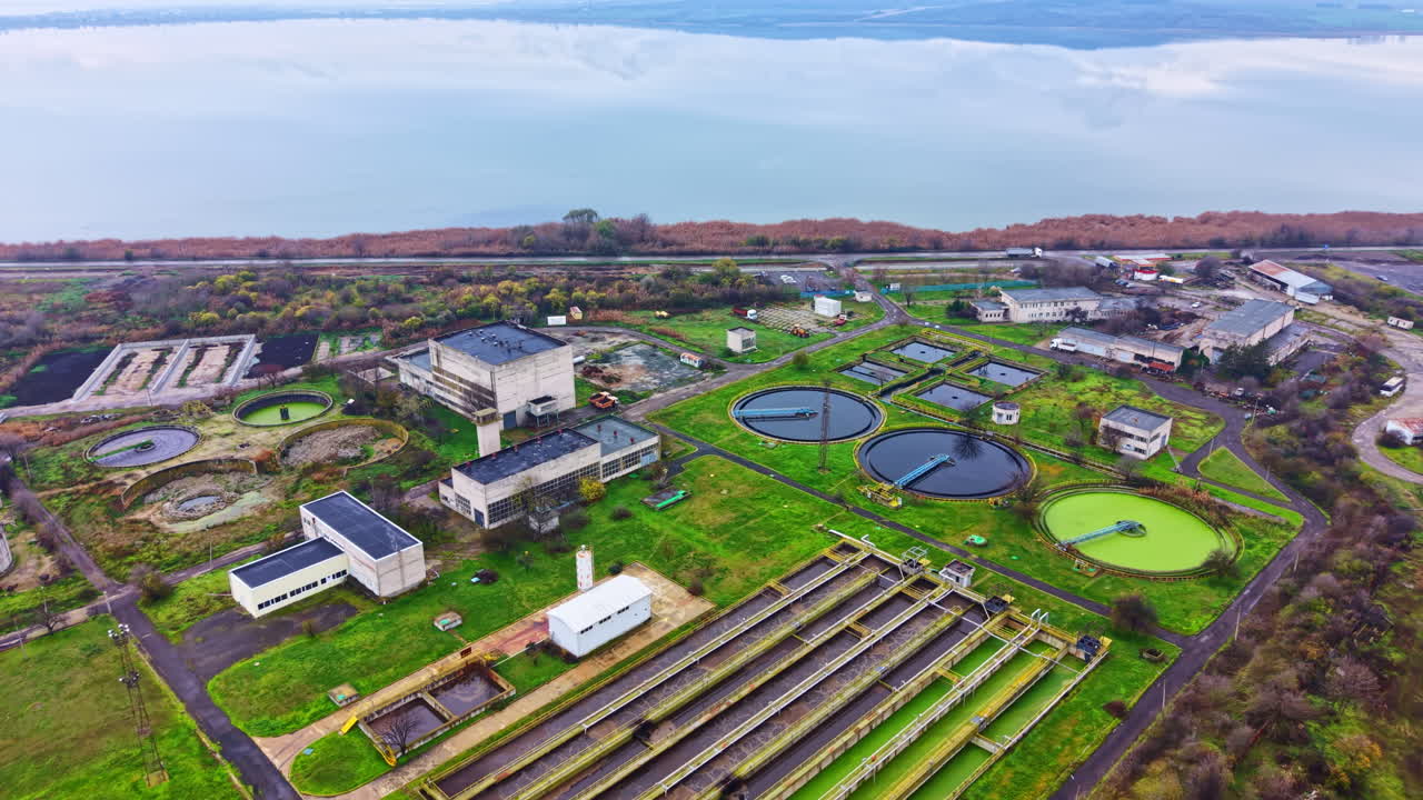 Wastewater treatment facility located near a body of water with various circular tanks visible in the area during daytime