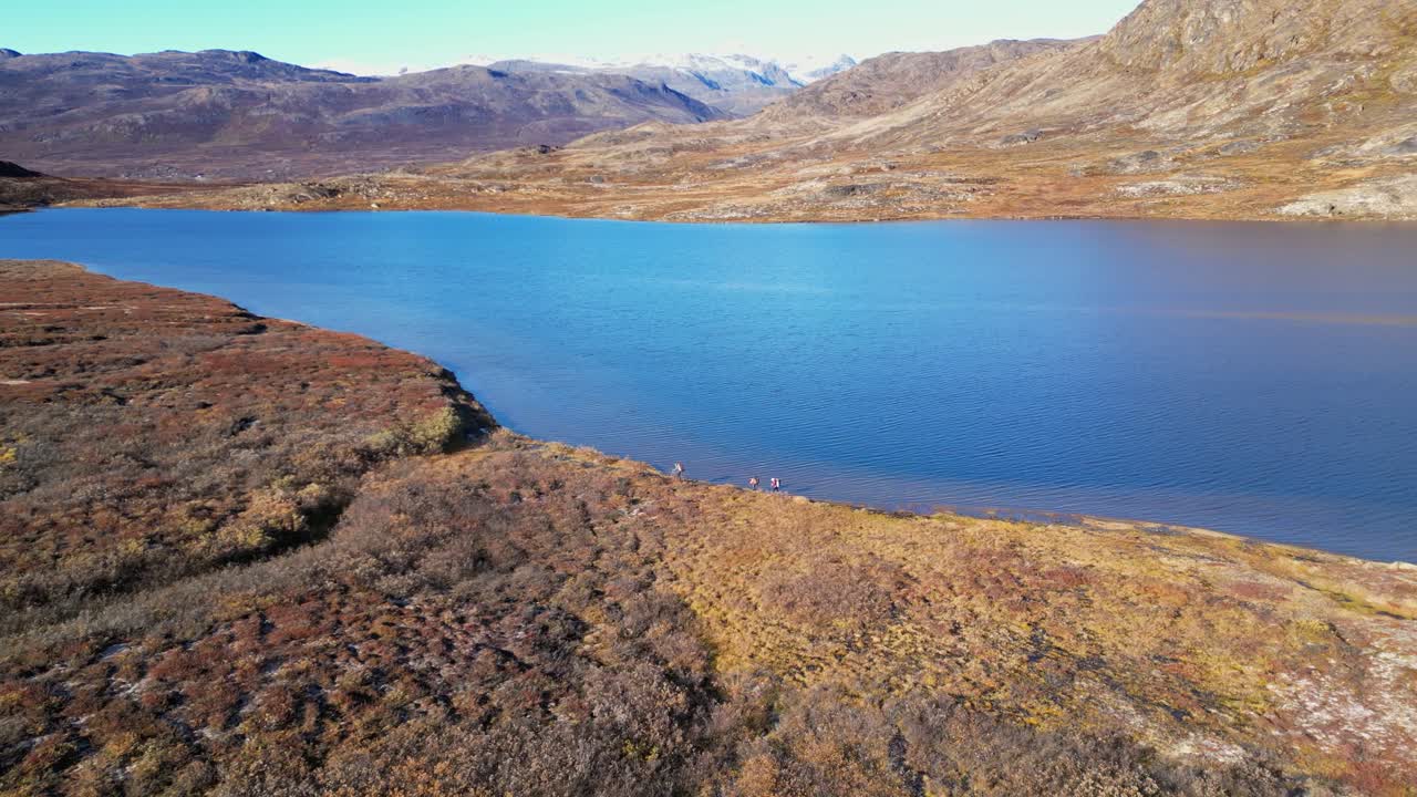 Hikers walk along arctic lake in golden rugged Greenland arctic tundra