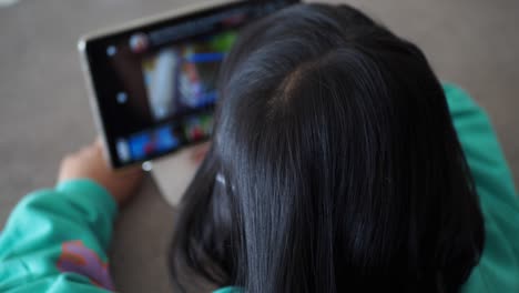 Rear-view-of-child-using-digital-tablet-sitting-on-chair,-selective-focus-,