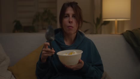 mujer comiendo helado o cereal en el sofá por la noche