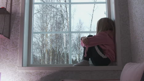 Blonde-Caucasian-girl-sitting-pensively-on-windowsill