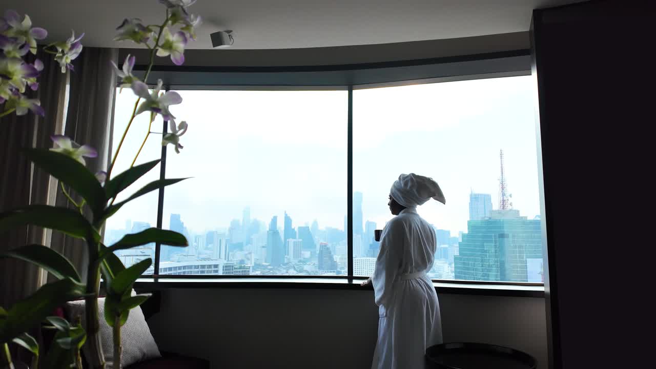 Woman in robe enjoys skyline view from hotel in Bangkok, relaxing atmosphere