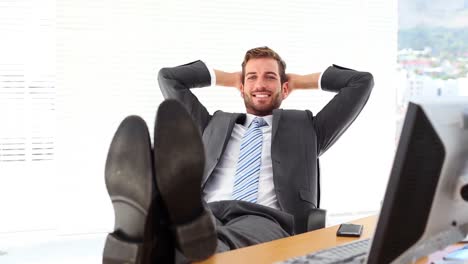 Relaxed-businessman-putting-his-feet-up-smiling-at-camera