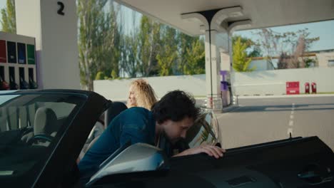 A-curly-brunette-guy-in-a-denim-jacket-gets-out-of-a-gray-convertible-and-refuels-the-car