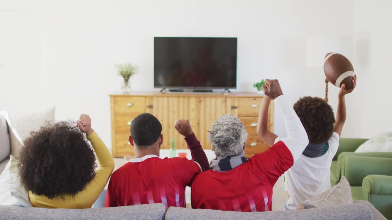 vista trasera de una familia de varias generaciones animando mientras ven deportes en la televisión en casa